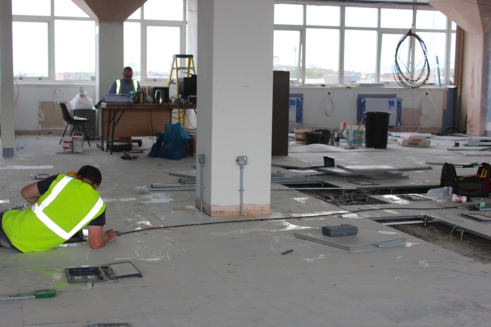 A man in yellow vest standing on the floor of an office.